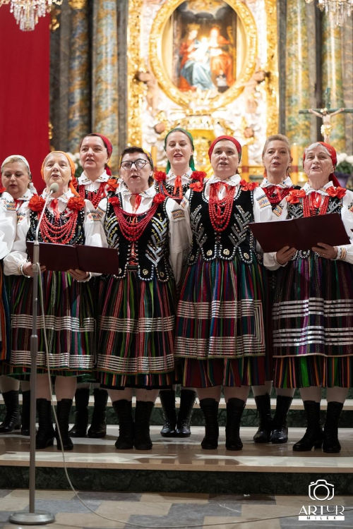 Dziewięć śpiewających pań ubranych w stroje ludowe. Za nimi widać obraz św. Anny i jej Rodziców oraz Tabernakulum.